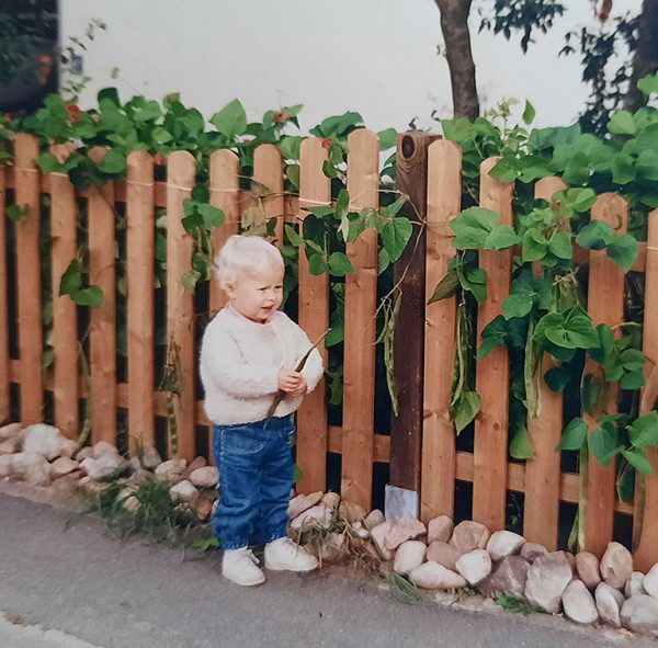 Kirsikka Lansmann im Kleinkindalter steht vor einem Zaun